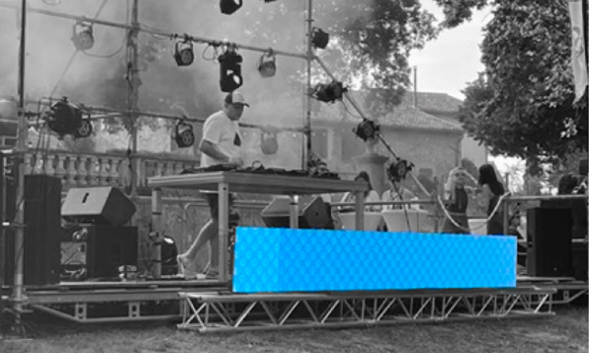 A DJ booth outdoors in black and white, with the LED panel on its front lit in blue with the pattern