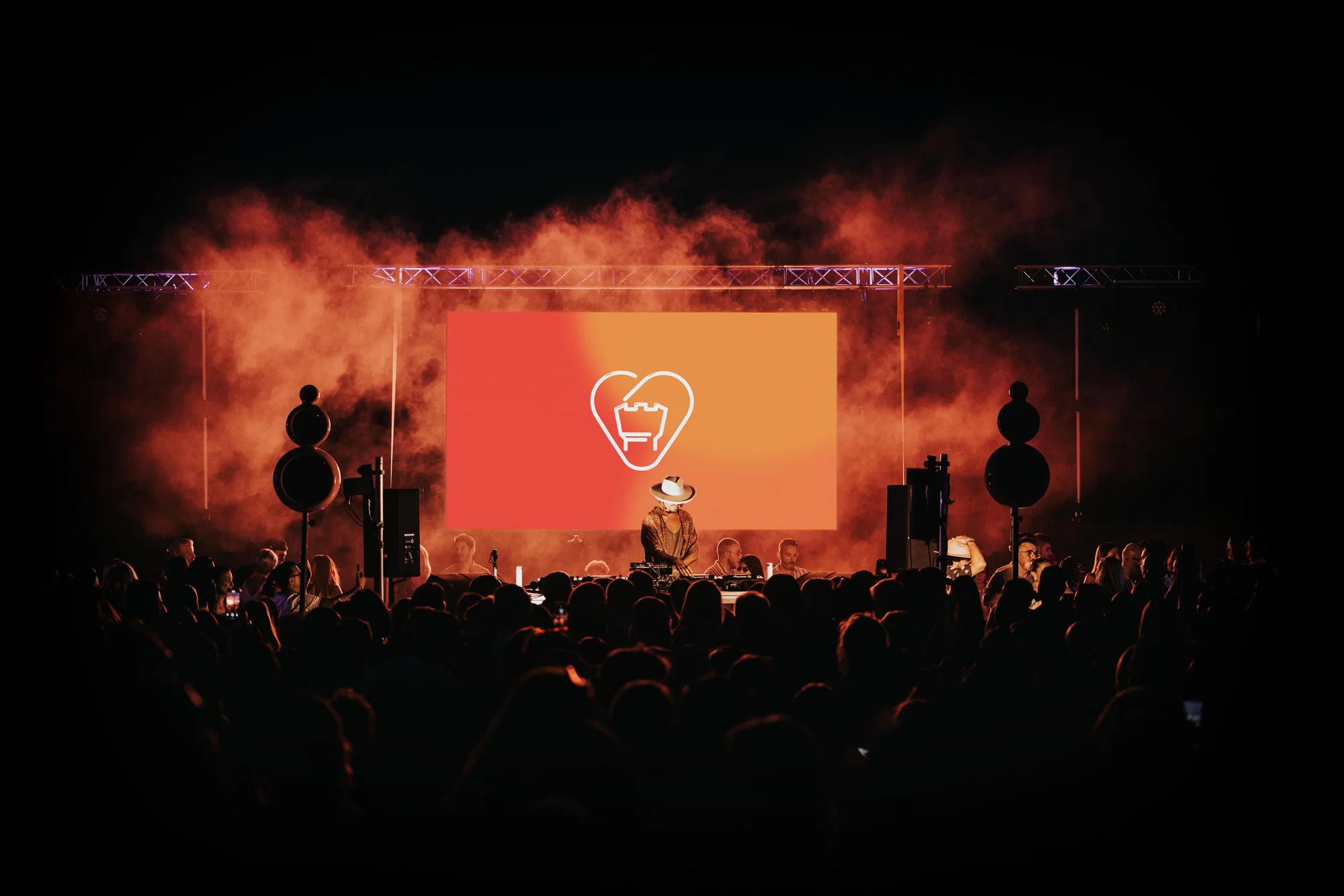 The stage at night in orange smoke, the mark in white on the screen, the crowd in silhouette